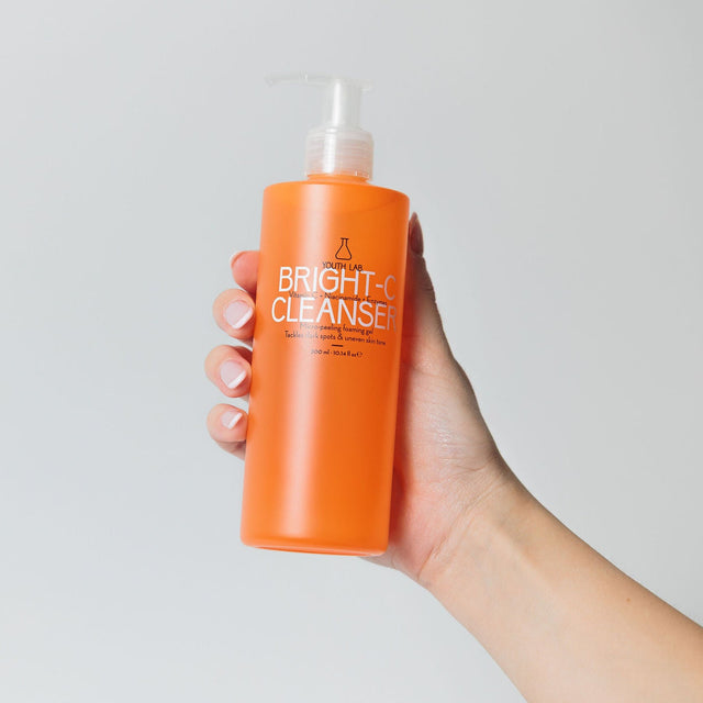 Hand holding an orange bottle labeled 'Bright Cleanser' against a light gray background