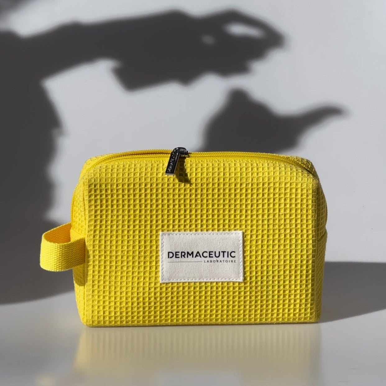 Yellow toiletry bag with Dermaceutic label on a white background