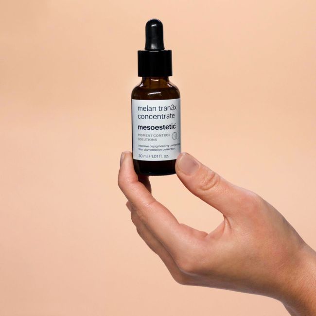 Hand holding a bottle of melan tran3x concentrate against a beige background