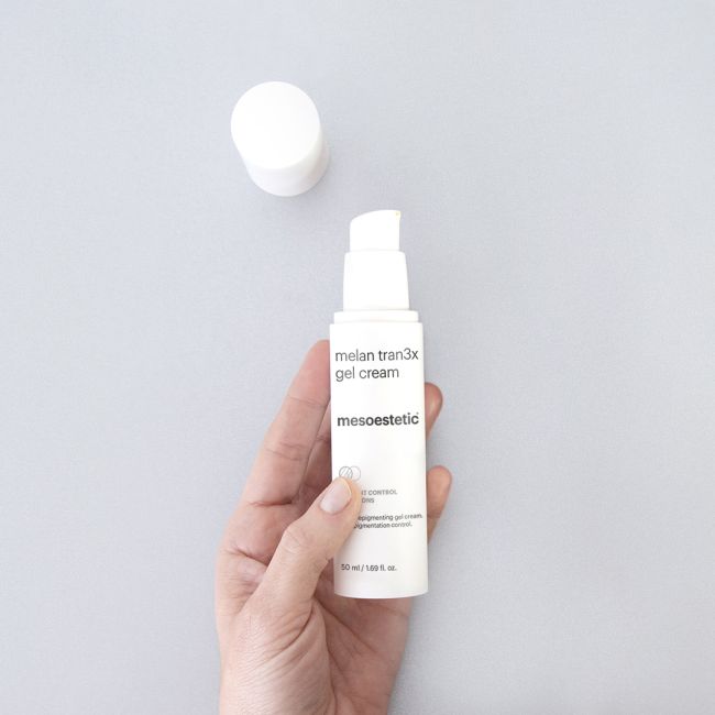 Hand holding a bottle of Mesoestetic melan tran3x gel cream against a light gray background