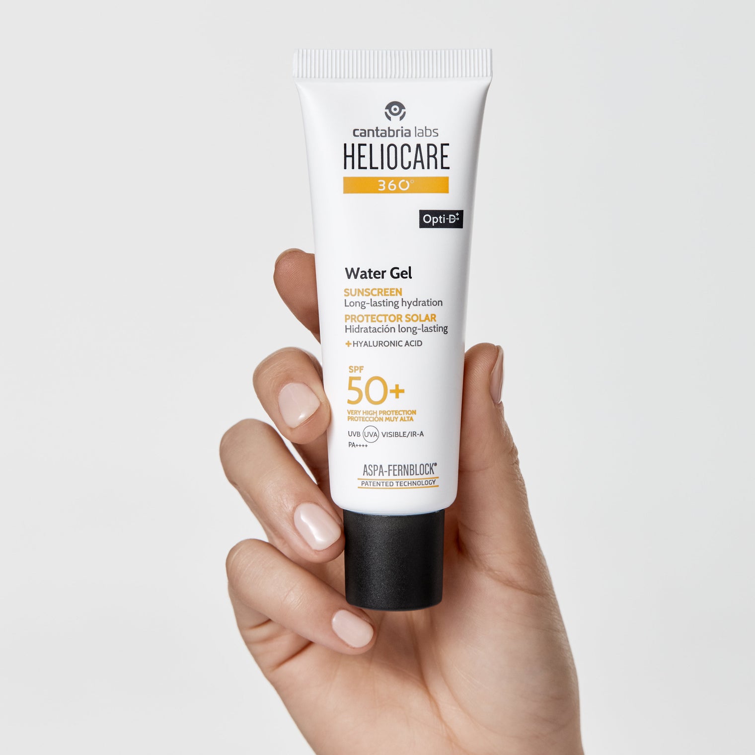 Hand holding a tube of Heliocare Water Gel sunscreen on a light gray background